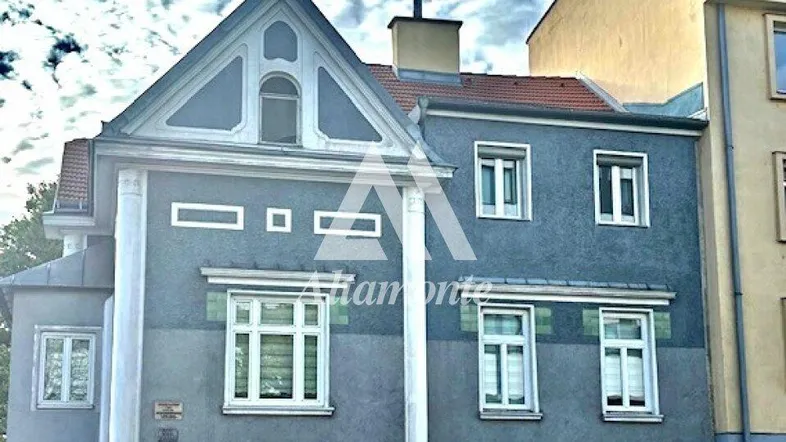Historische Fassade eines Gebäudes in Grau mit weißen Fensterrahmen und dekorativen Elementen.