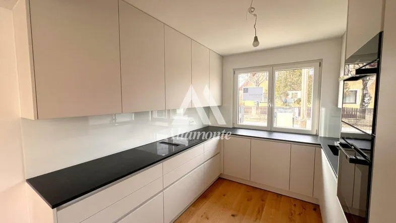 Moderne Küche mit weißen Schränken, dunkler Arbeitsplatte und Holzboden, gut beleuchtet durch ein Fenster.