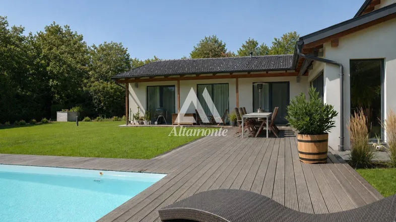 Große Holzterrasse mit Pool und Gartenmöbeln, umgeben von viel Grün und dem Haus.