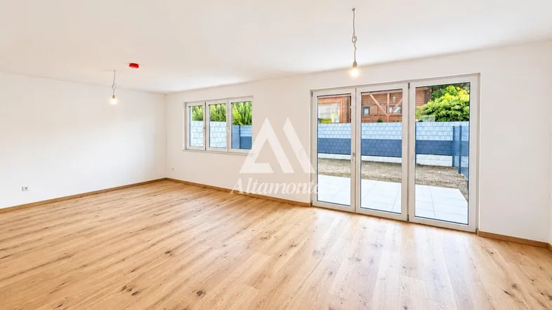 Helles, leeres Wohnzimmer mit Holzboden und Zugang zur Terrasse und zum Garten.