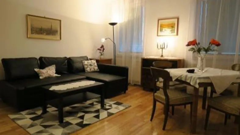 Gemütlicher Wohn- und Essbereich mit dunklem Sofa, Esstisch und hellem Parkettboden.