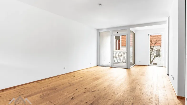 Helles Zimmer mit Holzboden und Zugang zu einem kleinen Balkon, ideal als Wohn- oder Schlafbereich.