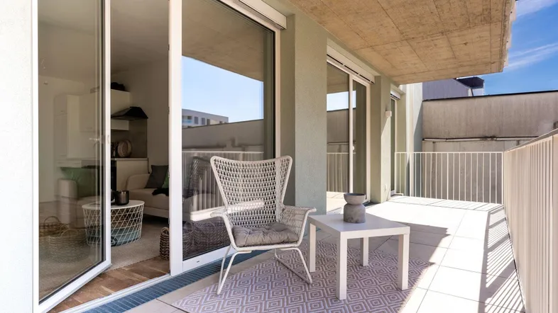 Heller Balkon mit Fliesenboden, Sitzgelegenheiten und Blick auf die Umgebung.