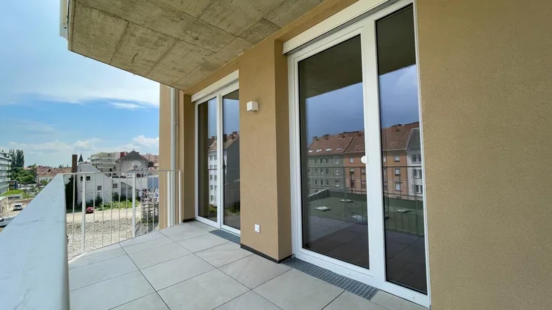 Geräumiger Balkon mit Fliesenboden und Blick auf die umliegenden Wohngebäude unter bewölktem Himmel.