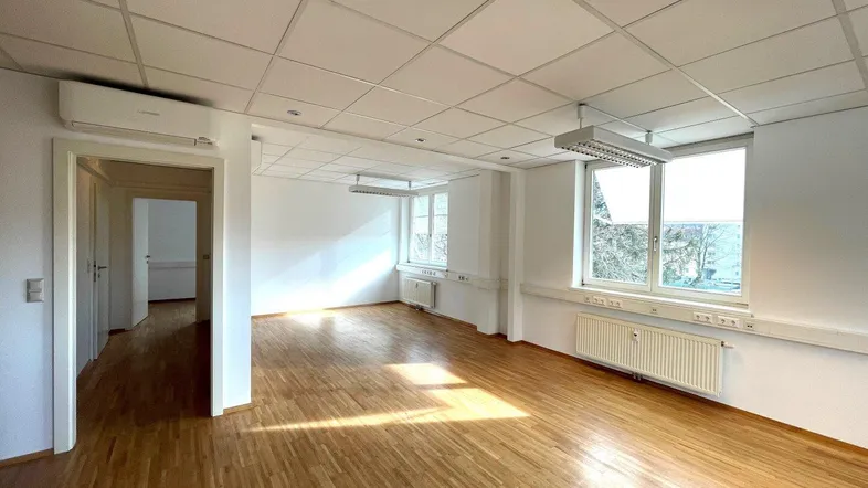 Geräumiges und helles Büro mit Holzparkettboden, großen Fenstern und Klimaanlage für angenehmes Raumklima.
