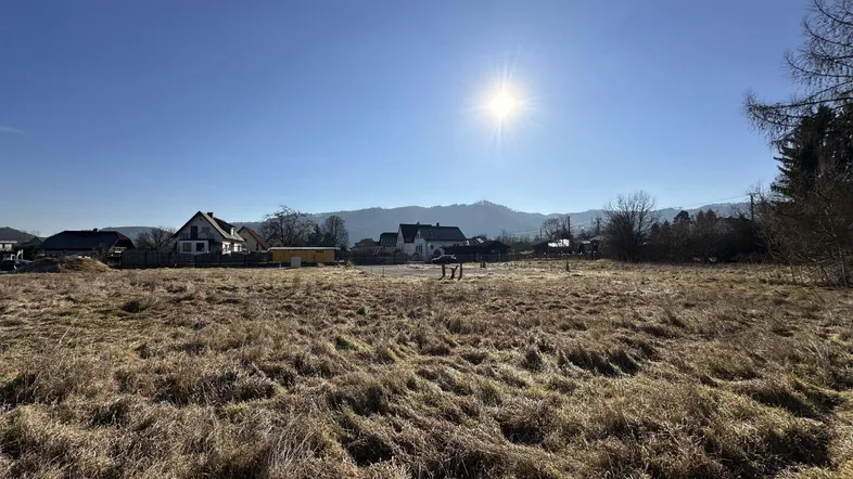 Sonniges Grundstück mit Blick auf die umliegende Landschaft und Berge, umgeben von vereinzelten Häusern.