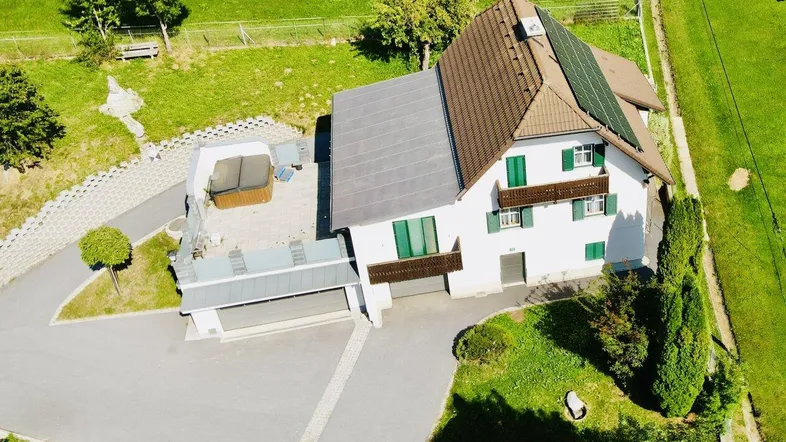 Luftaufnahme des Hauses mit Photovoltaikanlage, Whirlpool auf der Terrasse und grüner Umgebung.
