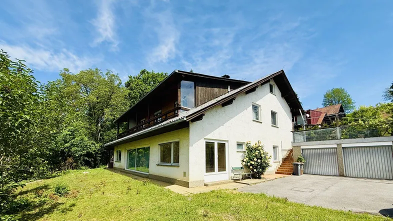 Weißes Einfamilienhaus mit Satteldach, umgeben von viel Grün und einem Vorgarten.