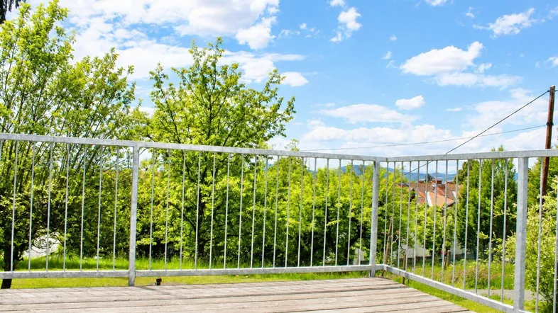 Holzterrasse mit Metallgeländer bietet einen weiten Blick auf grüne Bäume und die Umgebung.