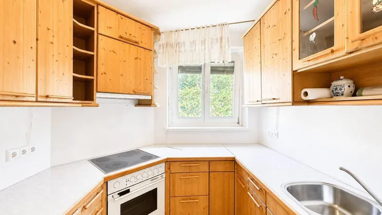 Kleine Küche mit Holzschränken, weißer Arbeitsplatte und Fenster mit Blick ins Grüne.