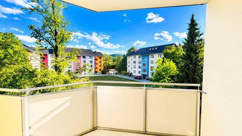 Heller Balkon mit moderner Verglasung und weitem Blick auf die umliegenden Gebäude und viel Grün.