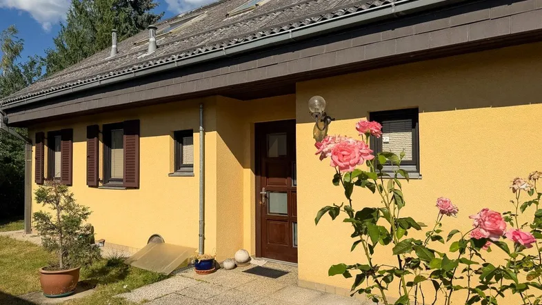 Gelbe Hausfassade mit brauner Eingangstür und blühenden Rosen im Vorgarten.