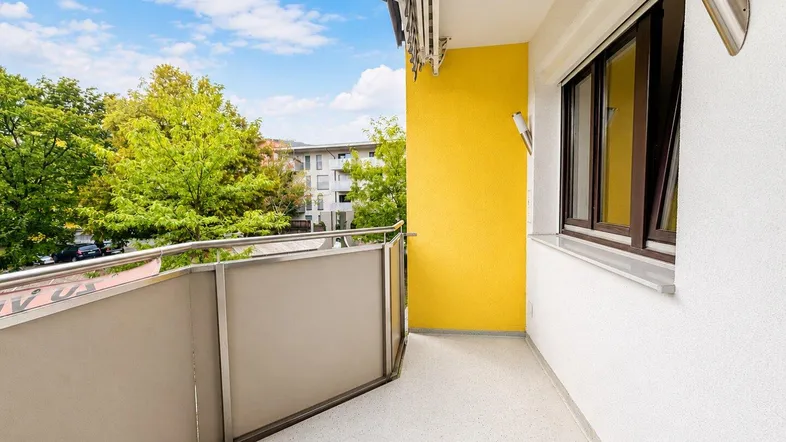Heller Balkon mit gelber Wand und Blick ins Grüne, ideal zum Entspannen im Freien.