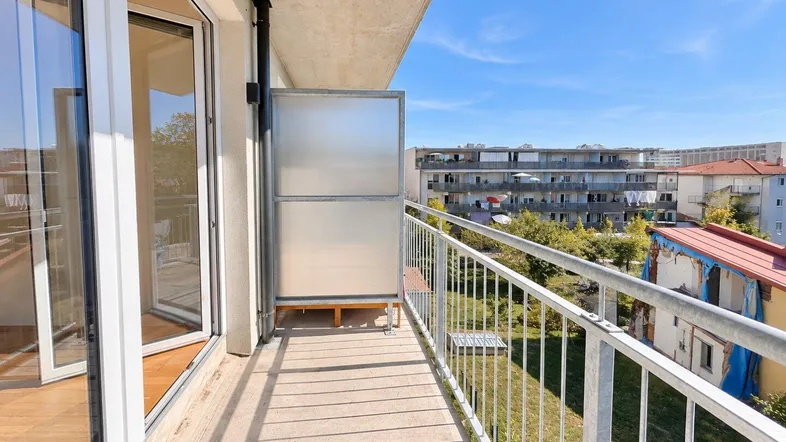 Heller Balkon mit Metallgeländer und Blick auf die umliegenden Gebäude und Bäume.