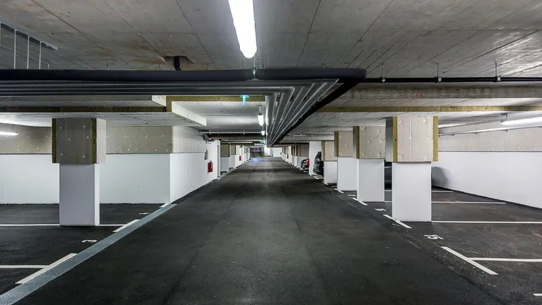 Tiefgarage mit Betonwänden und -decken, ausgestattet mit Leuchtstofflampen und markierten Parkplätzen.