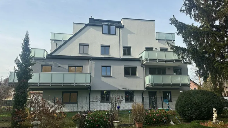 Modernes Mehrfamilienhaus mit Balkonen und gepflegtem Gartenbereich im Vordergrund.