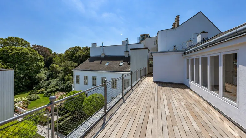 Große Holzterrasse mit Metallgeländer und Blick auf den Garten und umliegende Gebäude.