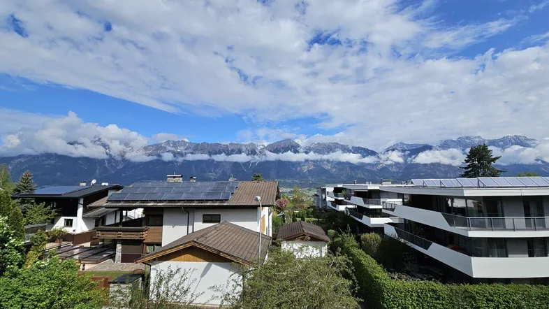 Blick auf die umliegende Berglandschaft mit Wohngebäuden und blauem Himmel.