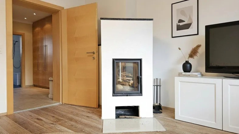 Gemütliches Wohnzimmer mit modernem Kaminofen, hellem Parkettboden und Zugang zu weiteren Räumen.