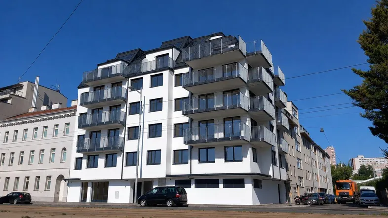 Modernes Apartmentgebäude mit Balkonen, Mansarddach und großen Fenstern an einer städtischen Straße.