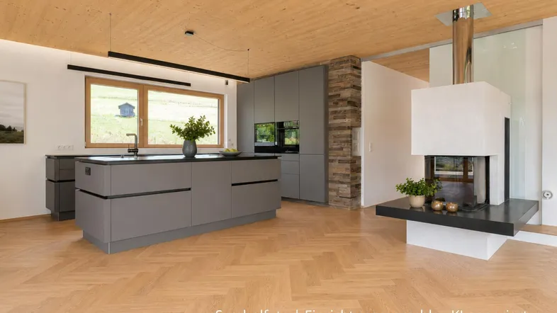 Moderne Küche mit grauen Schränken, Kochinsel und Holzboden, offen zum Wohnbereich mit Kamin.