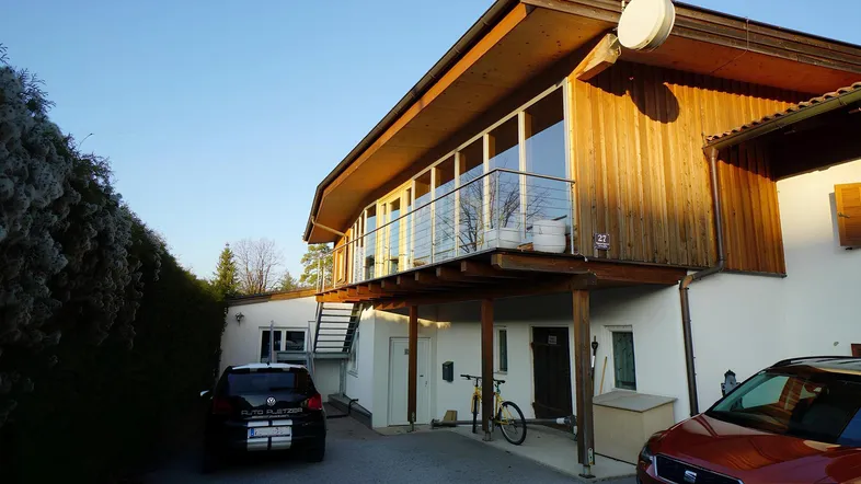 Modernes Gebäude mit Holzfassade, großem Balkon und Stellplätzen im Freien bei Sonnenuntergang.