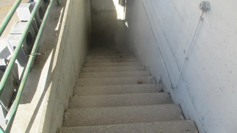 Betontreppe führt hinunter zu einem Untergeschoss oder einer Tiefgarage, ausgestattet mit einem stabilen Metallgeländer.