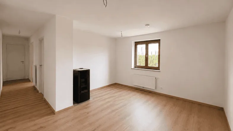 Helles, leeres Zimmer mit Laminatboden und einem modernen Kaminofen, bereit zur individuellen Gestaltung.
