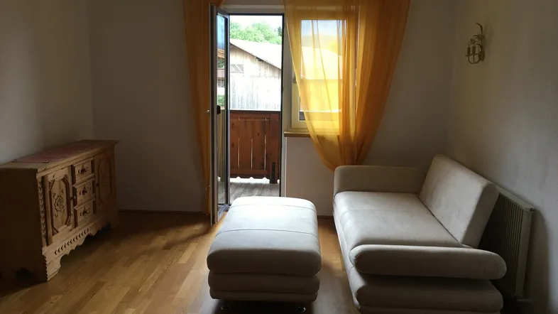 Helles Wohnzimmer mit Holzboden, beigem Sofa und Zugang zu einem kleinen Balkon.