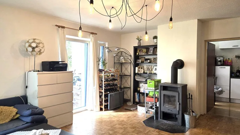 Gemütliches Wohnzimmer mit Kaminofen, Parkettboden und Zugang zum Balkon.