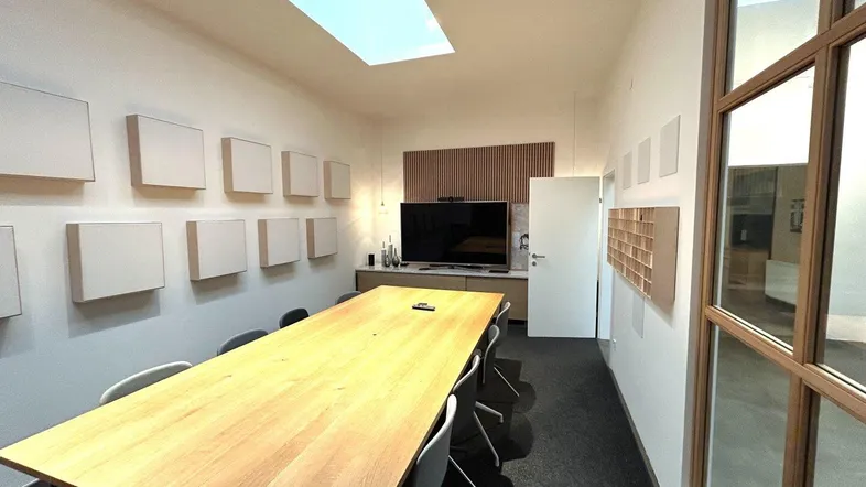 Modernes Besprechungszimmer mit großem Holztisch, Deckenfenster und schallabsorbierenden Wandpaneelen.