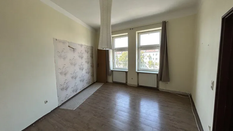 Leeres Zimmer mit Laminatboden, zwei Fenstern und teilweise entfernter Tapete, bereit zur Renovierung.