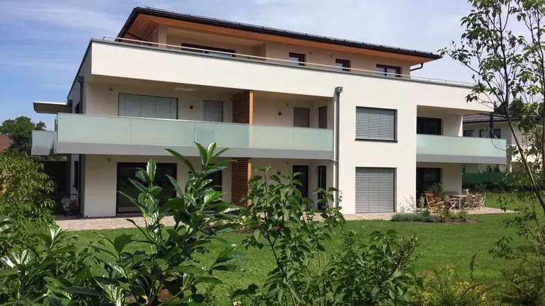 Modernes Mehrfamilienhaus mit weißer Fassade, Balkonen und gepflegtem Gartenbereich.