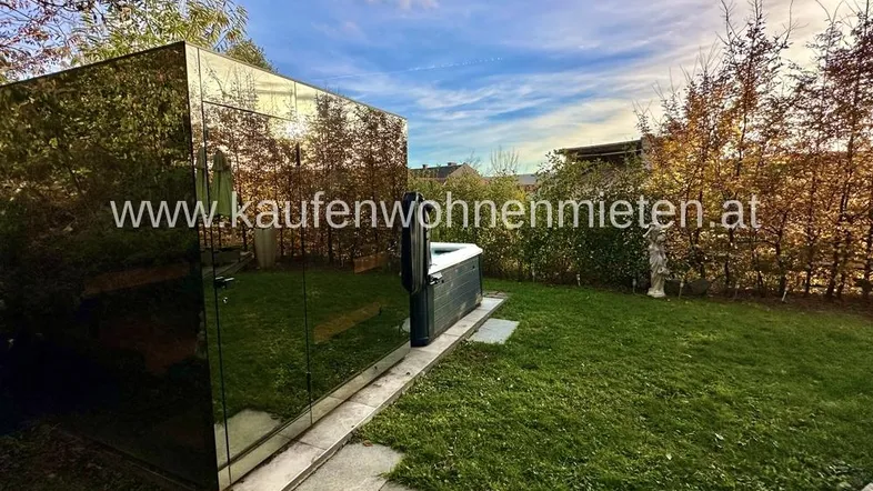 Moderner Gartenbereich mit Whirlpool und einer spiegelnden Gartenhütte unter blauem Himmel.