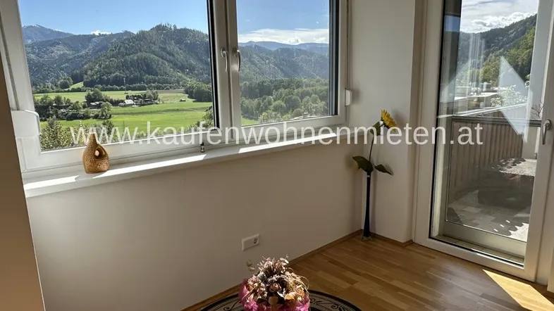 Helles Zimmer mit großen Fenstern, die einen weiten Blick auf die Berge und grüne Landschaft bieten.