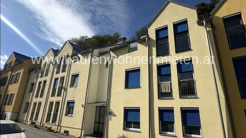 Mehrere moderne Wohngebäude mit gelber Fassade und blauen Fensterläden unter blauem Himmel.