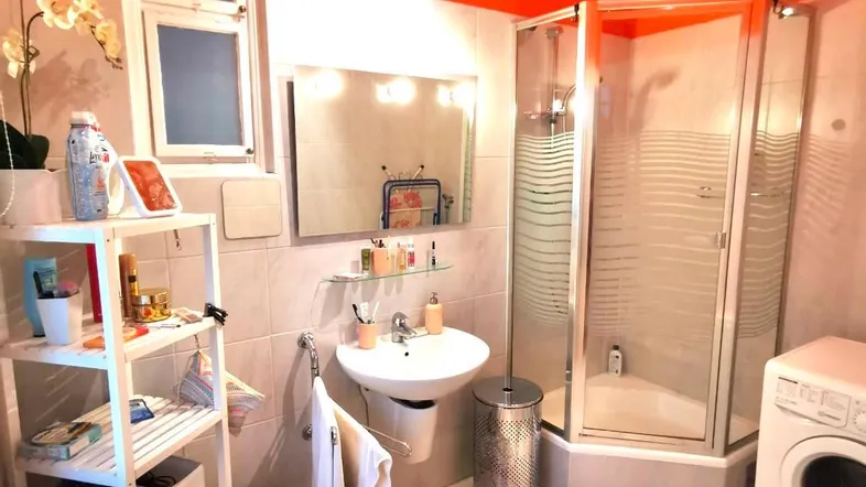Helles Badezimmer mit orangefarbener Decke, Duschkabine und Waschmaschine.