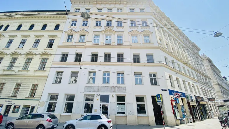 Das Eckgebäude präsentiert sich als klassisches Mehrfamilienhaus mit Geschäften im Erdgeschoss und Wohnungen darüber.
