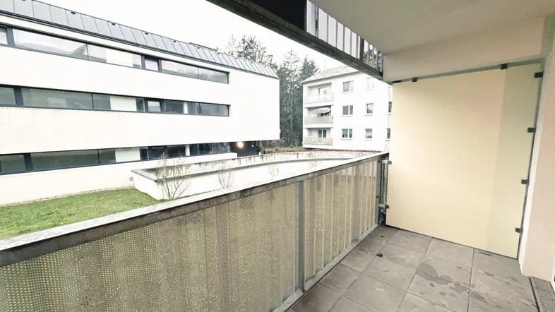 Balkon mit Fliesenboden und Blick auf die umliegenden Gebäude und eine kleine Grünfläche.
