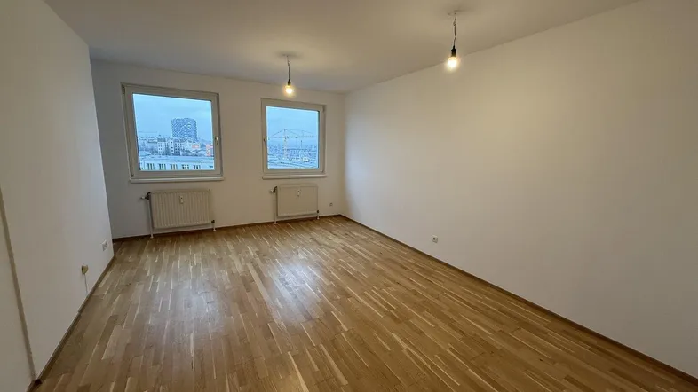 Helles Zimmer mit Parkettboden und zwei Fenstern, die einen Blick auf die Stadt bieten.