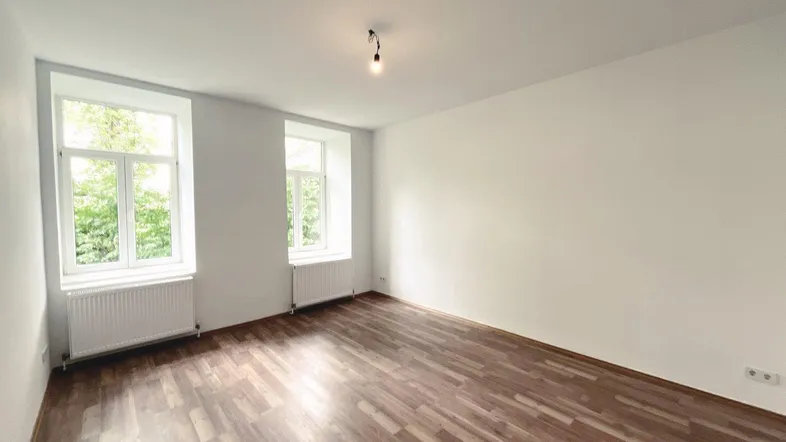 Helles Zimmer mit Laminatboden und zwei großen Fenstern, ideal als Wohn- oder Schlafzimmer.
