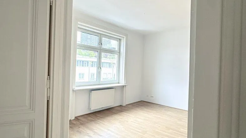 Helles, leeres Zimmer mit Parkettboden und großem Fenster, bereit zur individuellen Gestaltung.