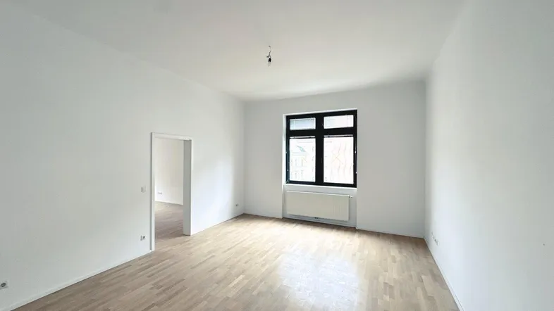Helles, leeres Zimmer mit Parkettboden und weißen Wänden, bereit zur individuellen Gestaltung.
