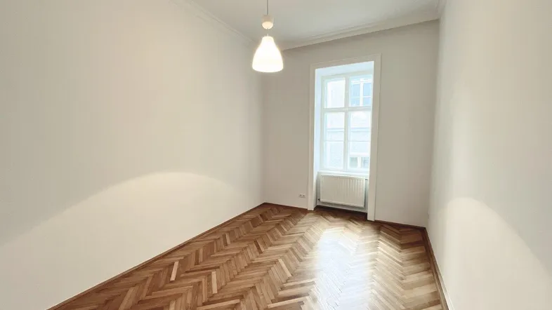 Helles Zimmer mit klassischem Fischgrätparkettboden und einem großen Fenster.
