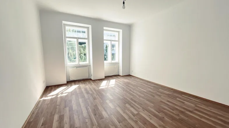 Heller, leerer Raum mit zwei großen Fenstern und modernem Laminatboden.
