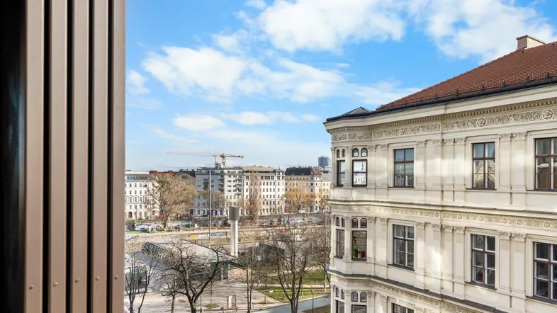 Blick aus dem Fenster auf eine belebte Stadtstraße mit historischen Gebäuden und einem Baukran am Horizont.