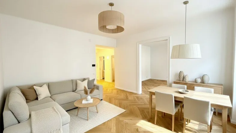 Heller, offener Wohn-Essbereich mit modernem Sofa, Esstisch und Fischgrätparkettboden.