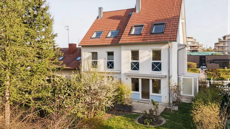 Außenansicht des Hauses mit Garten, Terrasse und Dachfenstern unter einem roten Ziegeldach.