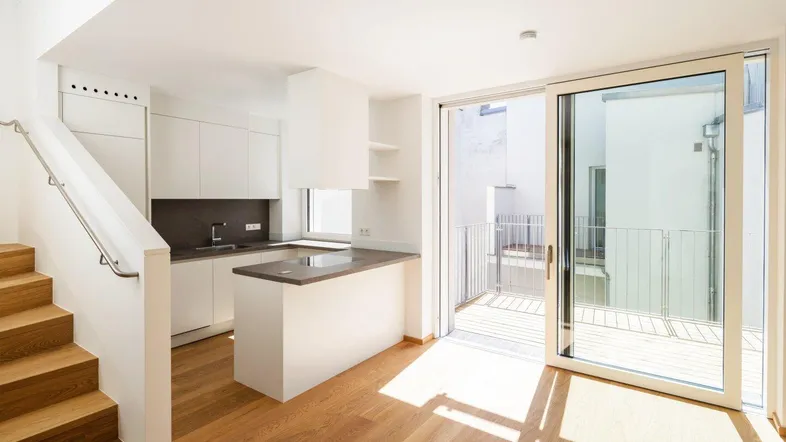 Helle, moderne Küche mit Kochinsel, Parkettboden und Zugang zu einem kleinen Balkon.