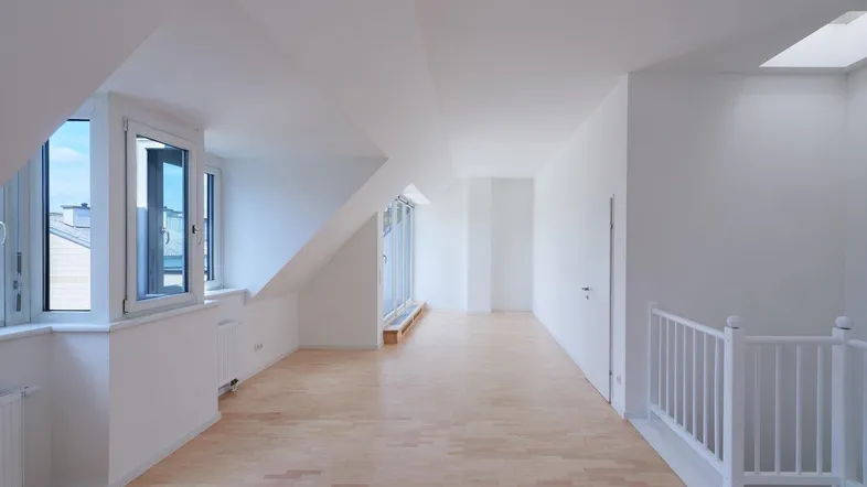 Helles Dachgeschosszimmer mit Holzboden, schrägen Wänden und Zugang zu einem Balkon.